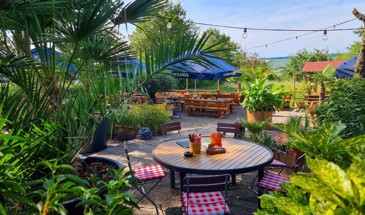 Sommerlicher Biergarten mit Palmen, Lichterketten und Blick ins Tal