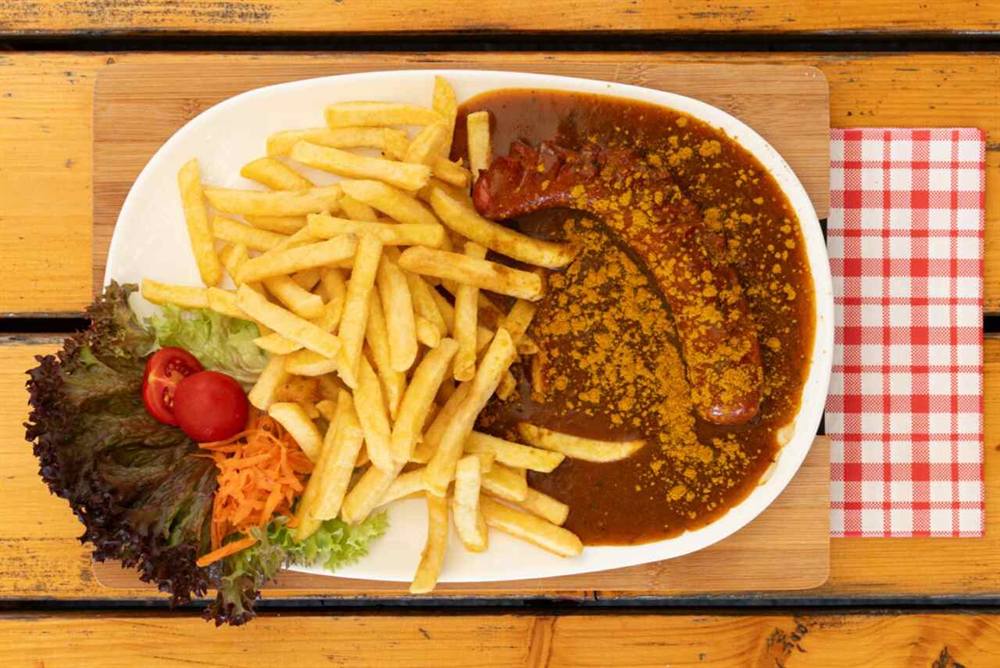 Currywurst mit Pommes und Salatgarnitur auf weißem Teller